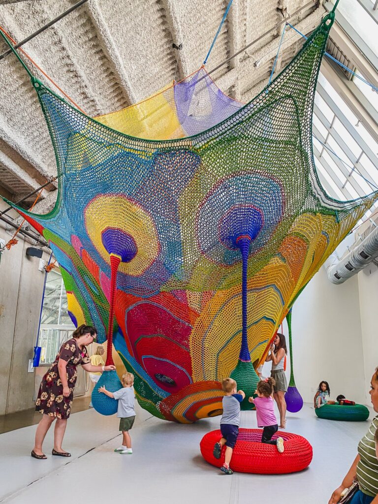 Children exploring a colorful net installation at The New Children’s Museum.